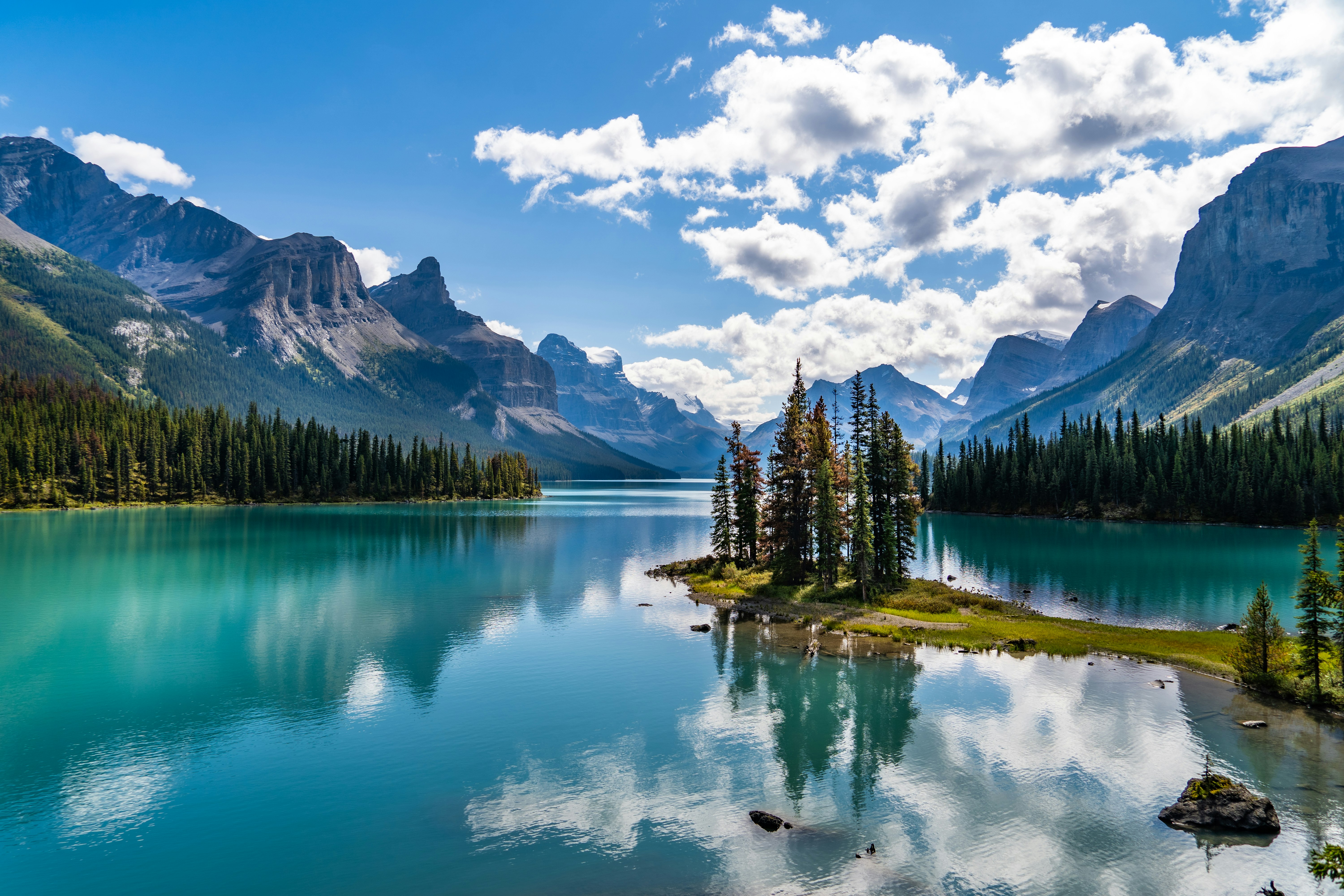 green trees near lake and mountains under blue sky during daytime